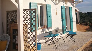 A white building with blue shutters, a tiled roof, and a patio with a table and chairs.