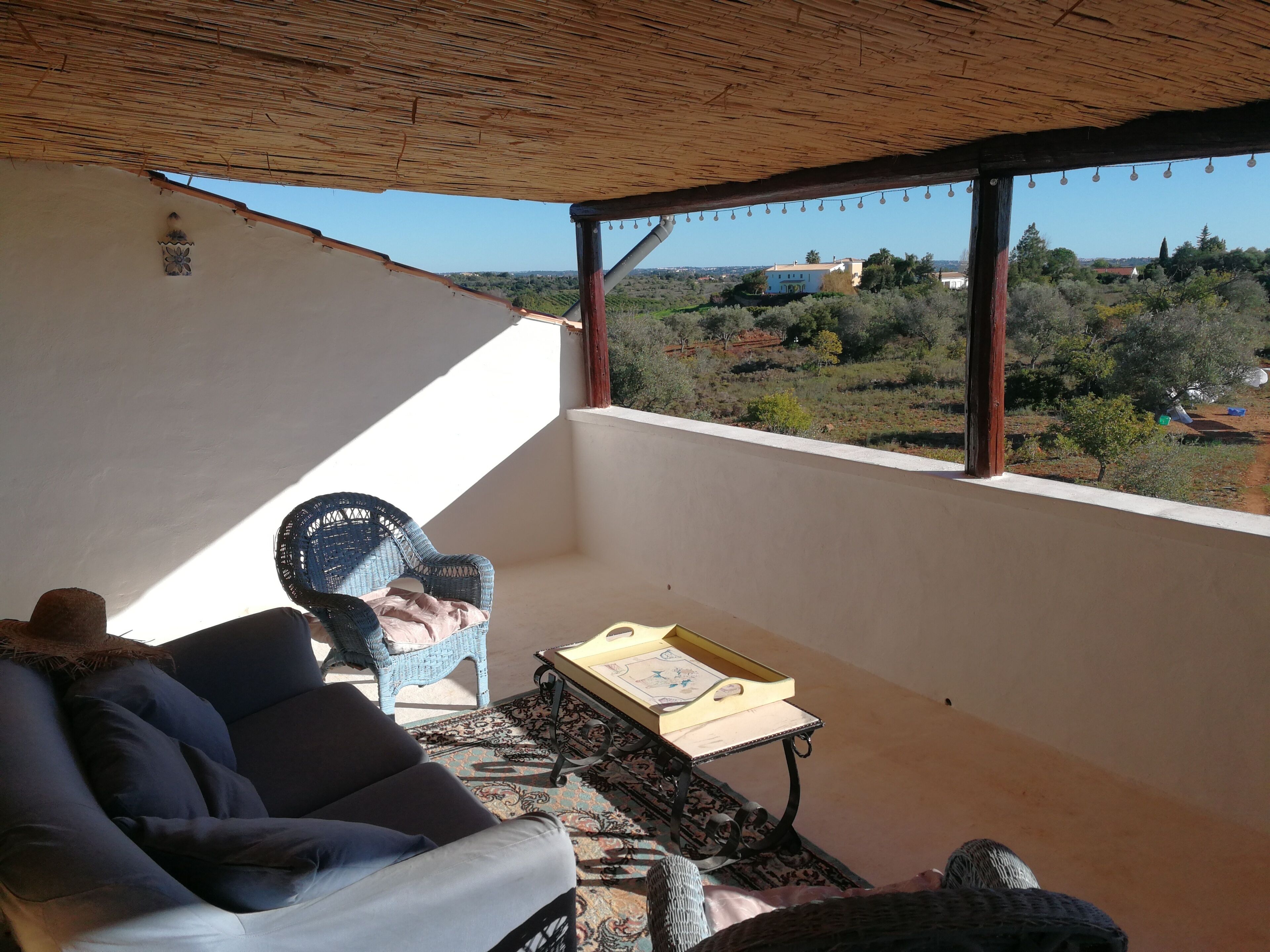 Un balcon avec un fauteuil en osier, un canapé et une petite table sur laquelle se trouve un plateau.