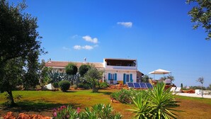 A two-story house with a garden in front, a pool area, and solar panels.