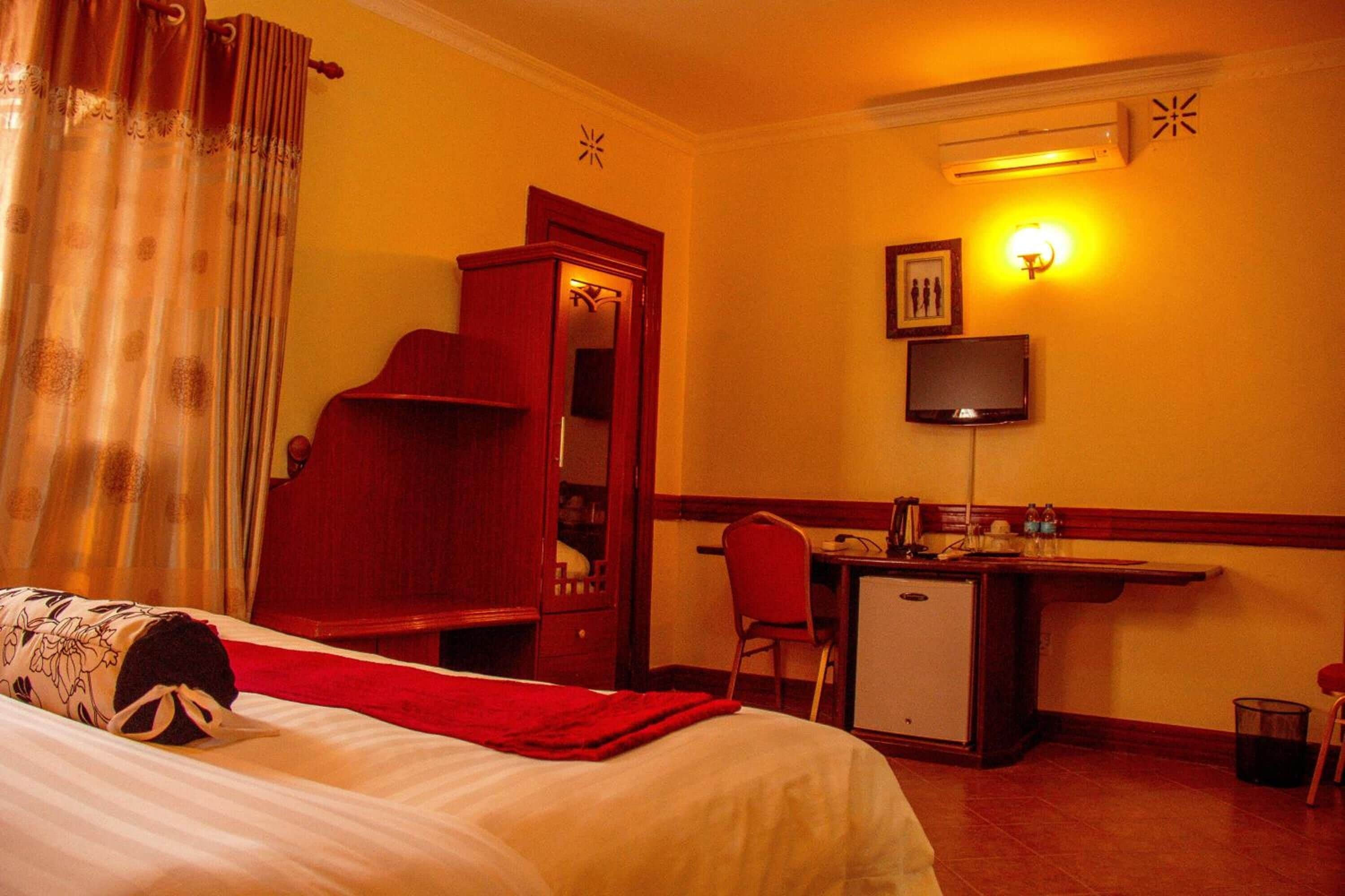 A hotel room with a bed, a desk, a chair, a television, and a small refrigerator.