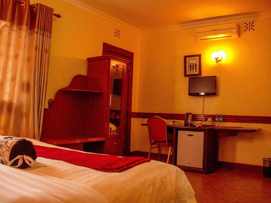 Quarto de hotel com cama, escrivaninha, cadeira, televisão e um pequeno frigorífico.