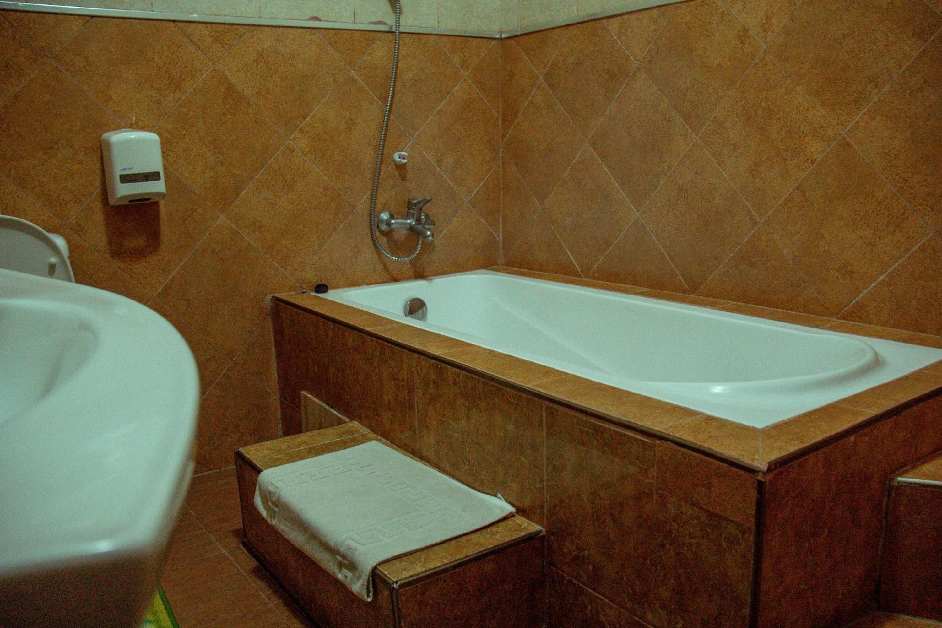 A bathroom with a bathtub, a toilet, and a hand soap dispenser.