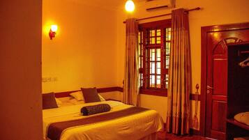 Quarto de hotel com cama, guarda-roupa, janela com cortinas e luminária na parede.