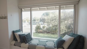 A room with a large window, a cushioned bench, and a view of a parking area.