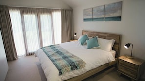 A bedroom with a large bed, two bedside tables, a nightstand, and a painting of a seascape.