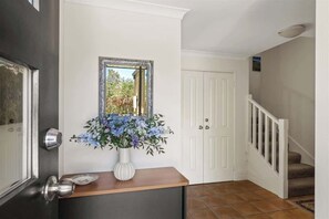 Un couloir avec une porte blanche, un miroir et un vase rempli de fleurs.