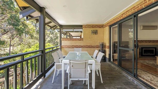 A covered patio with a dining table and chairs, a brick wall, and a sliding glass door leading to an interior space.
