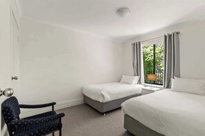 Une chambre d’hôtel avec deux lits, une chaise, une fenêtre avec des rideaux et un luminaire au plafond.