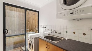 A laundry room with a washing machine, a sink, and a window with a view of a wooden deck.