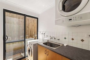 A laundry room with a washing machine, a sink, and a window with a view of a wooden deck.