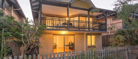 Ein zweistöckiges Haus mit Balkon, Holzzaun und Garten.