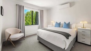 A hotel room with a bed, a chair, a nightstand, and a window with curtains.