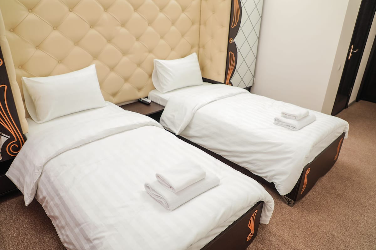 A hotel room with two single beds, each with a white duvet and a folded towel.