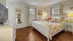 A bedroom with a wooden floor, a bed with floral bedding, a TV on a dresser, and a window with curtains. - Perfect 2 BR Condo in Princeton w Parking  (PRINCETON)