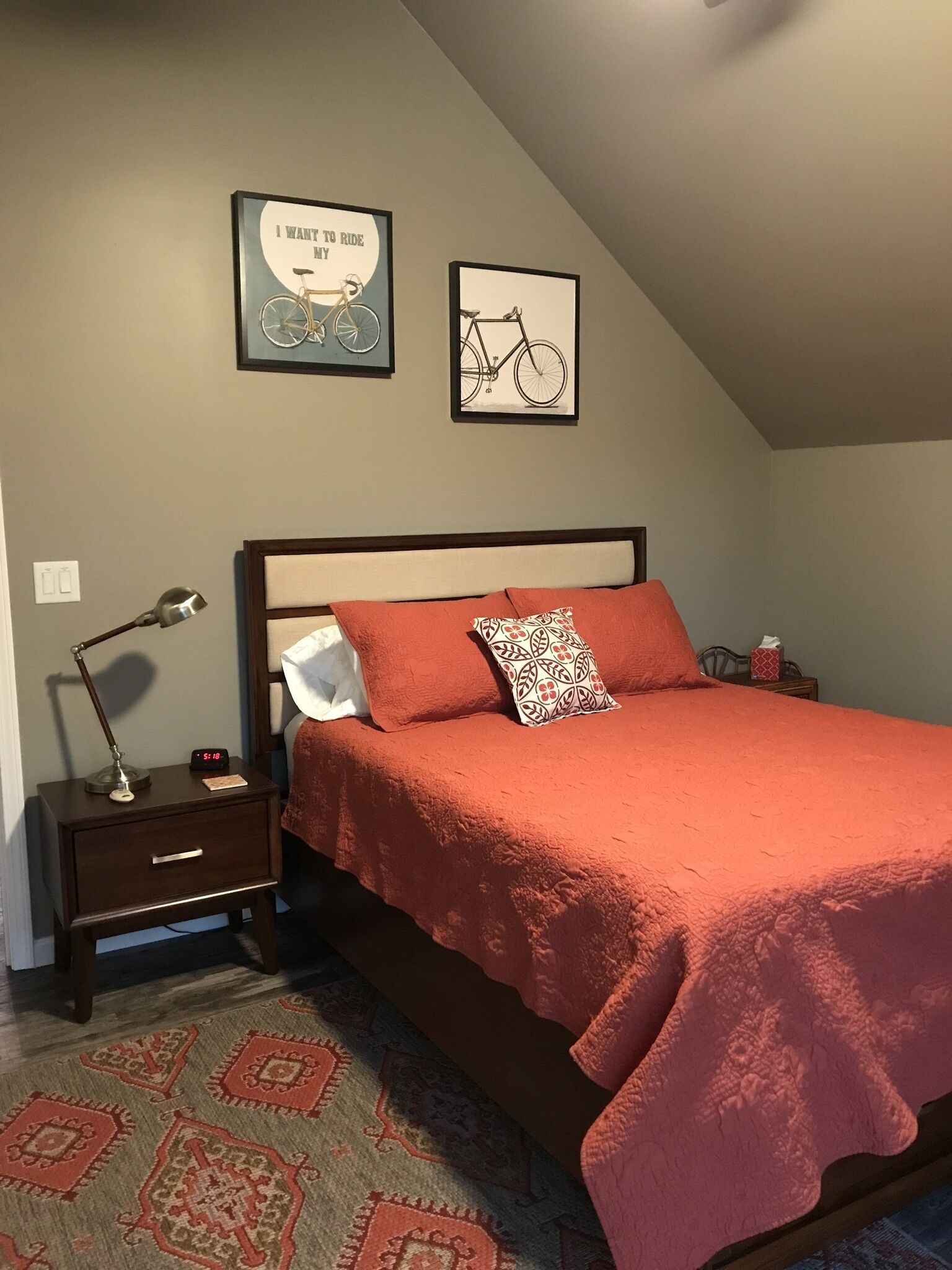 Une chambre à coucher avec un lit, une table de chevet, une lampe et deux tableaux encadrés accrochés au mur.