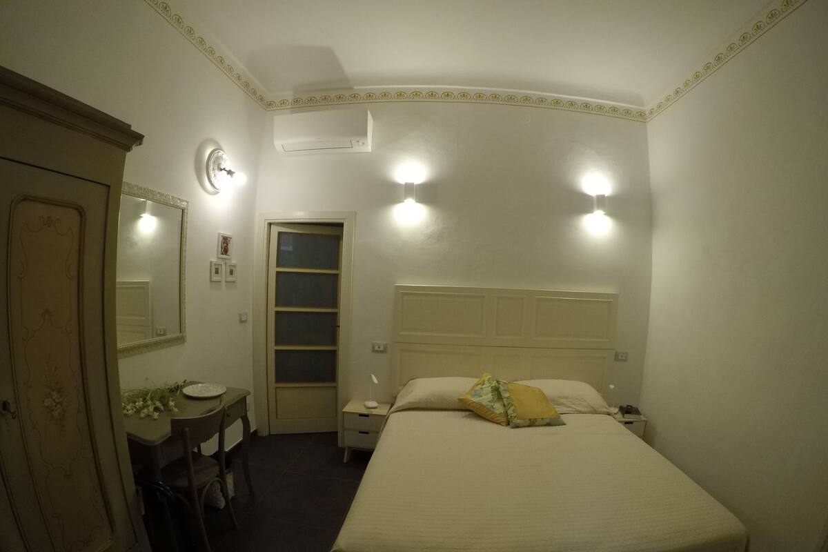 A bedroom with a bed, bedside table, nightstand, dresser, mirror, and an air conditioning unit.