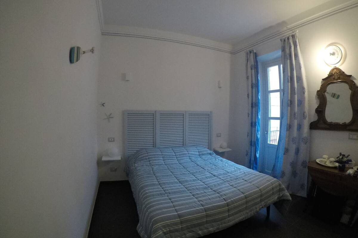A bedroom with a bed, a nightstand, a mirror, and a window with curtains.