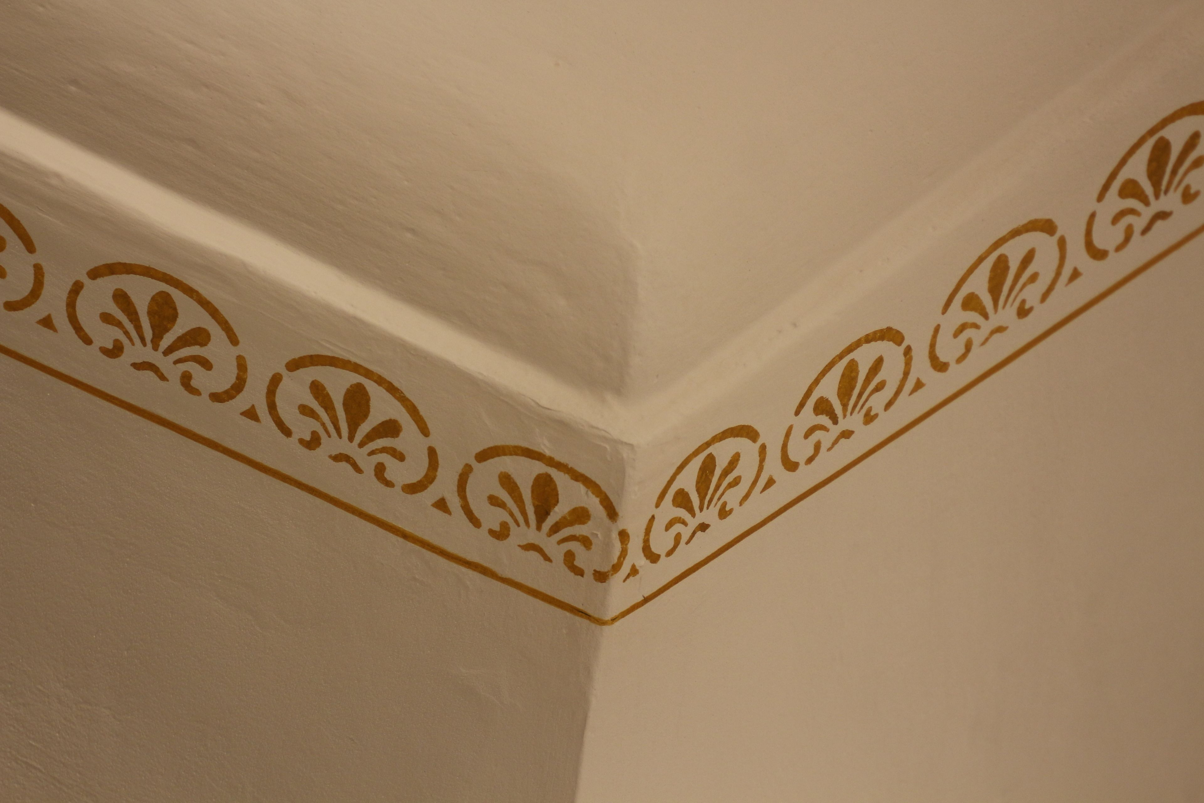 A corner of a room with a white ceiling and a decorative molding with a floral pattern.