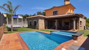 Una casa de piedra de dos pisos con piscina, un porche cubierto y un pequeño jardín.