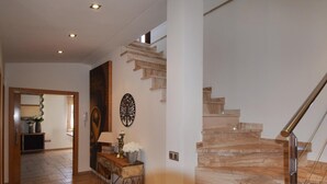 Un interior moderno con una escalera de mármol, una consola con objetos decorativos y una obra de arte en la pared.