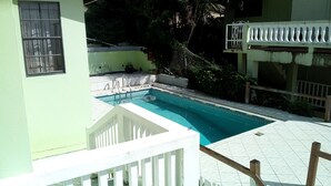 A swimming pool with a tiled deck, surrounded by a white fence and a building with a barred window. - Tranquil Ocean Views (Gros Islet)