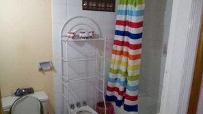 Um banheiro pequeno com parede revestida de azulejos brancos, vaso sanitário branco, prateleira branca e cortina de chuveiro listrada.