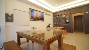 A modern hotel room with a glass dining table, wooden benches, a painting on the wall, a small shelf with decorative items, and a reception desk with a counter. - Coral Habitat (Magong)