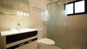 A modern bathroom with a glass shower enclosure, a white toilet, and a black and white vanity with a mirror. - Coral Habitat (Magong)