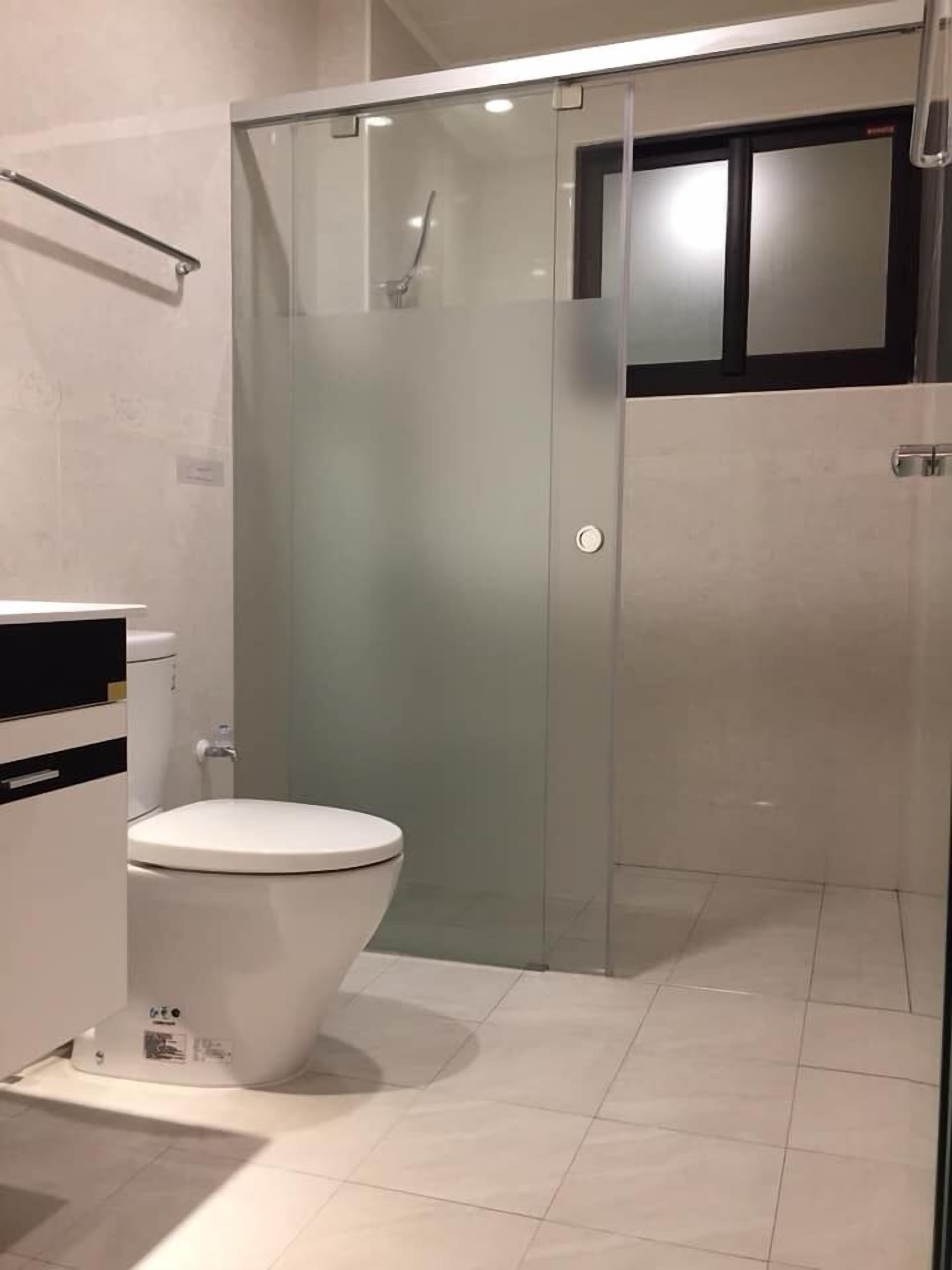 Uma casa de banho moderna com cabine de chuveiro em vidro, sanita branca e esguicho de chuveiro visível.