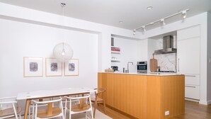 Una cocina moderna con armarios blancos, una isla de madera y un comedor con sillas blancas.