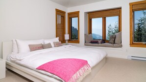 Un dormitorio moderno con una cama grande, un asiento junto a la ventana con cojines y vistas al exterior.