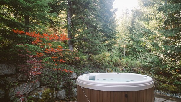Un jacuzzi en zona boscosa con pared de piedra y terraza de madera.