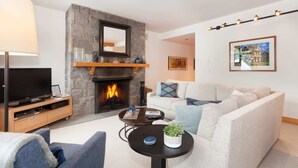 Ein Wohnzimmer mit Kamin aus Stein, einem Fernseher, einer Couch und einem Couchtisch.