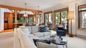 Ein modernes Wohnzimmer mit einer großen Eckcouch, einem Couchtisch und einem Essbereich mit Holzsäulen und einer grönen Spritzschutzwand.