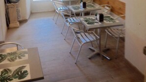 Un comedor con mesas y sillas, un banco de madera, un reloj en la pared y una puerta que da al exterior.