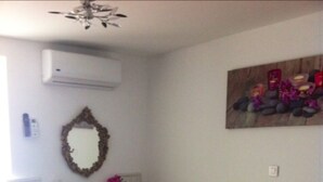 Un dormitorio con cama, escritorio, silla, espejo y aire acondicionado instalado en la pared.