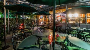 An outdoor cafe with tables and chairs, umbrellas, and a glass enclosure with plants. - Hotel Beverly (Mexico City)