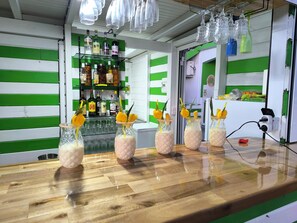 A bar area with a wooden counter, glasses, bottles, and a green and white striped wall.