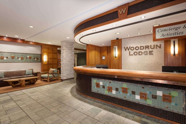 A reception area with a wooden counter, a sign for Woodrun Lodge, and a seating area with a bench and chairs.