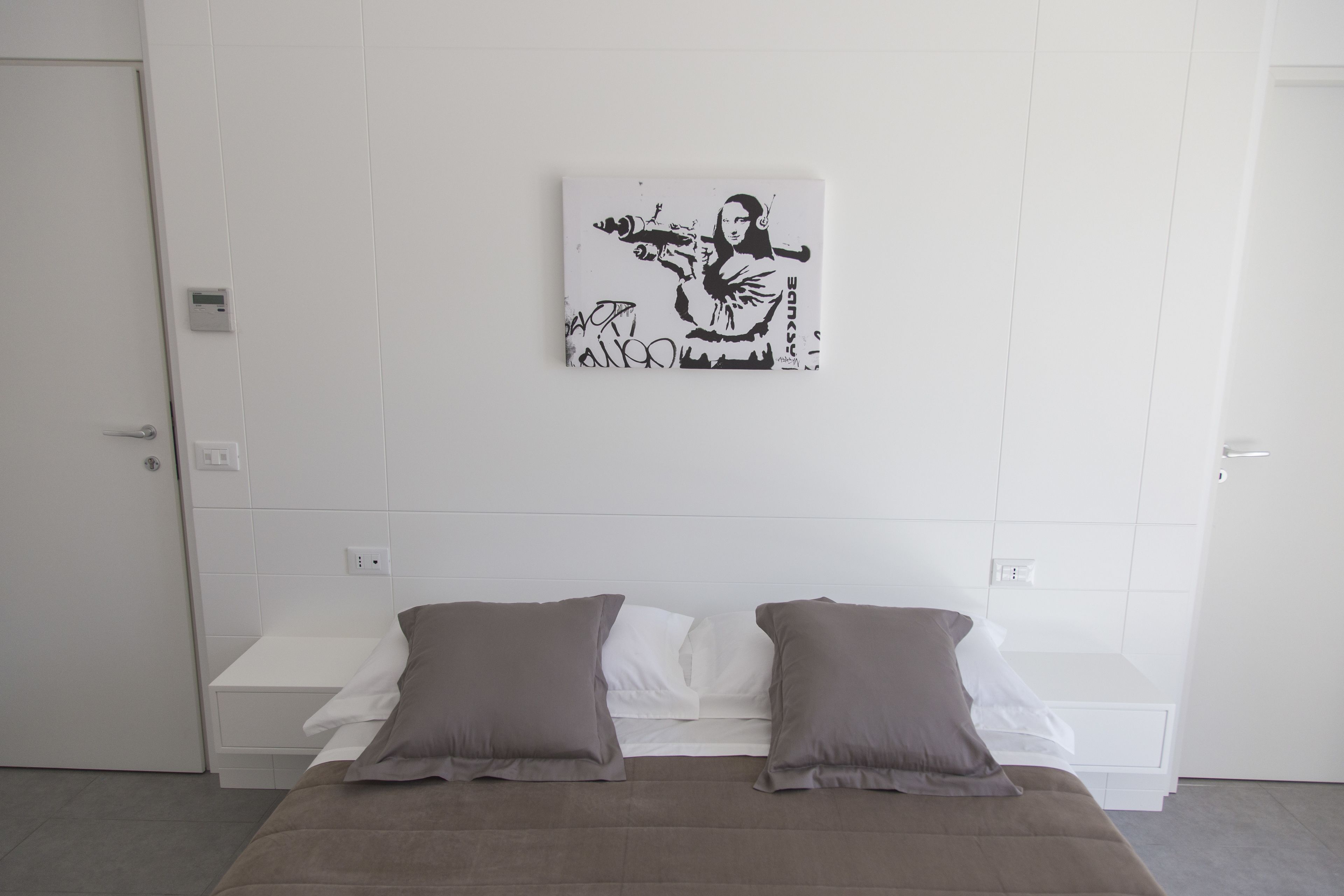 A bedroom with a bed, pillows, a wall-mounted artwork, and a bedside table.
