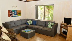 A living room with a grey sectional sofa, a coffee table, and a TV stand. - Rarotonga Island Villa 1 (Papaaroa)