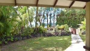 A covered outdoor area with a concrete path, surrounded by lush greenery and palm trees. - Rarotonga Island Villa 1 (Papaaroa)