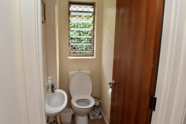 A small bathroom with a toilet, bidet, and a window with a decorative grille. - Rarotonga Island Villa 1 (Papaaroa)