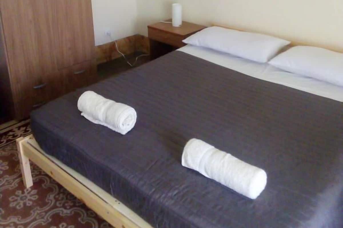 Un lit simple avec un matelas foncé et deux serviettes blanches roulées, posées dessus.