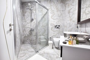 A modern bathroom with a glass-enclosed shower, a white toilet, and a vanity with a sink and various toiletries. - Siete Hotel (Antalya)