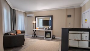 A modern hotel room with a sofa, a desk with a mirror, a minibar, and a flat-screen TV. - Siete Hotel (Antalya)