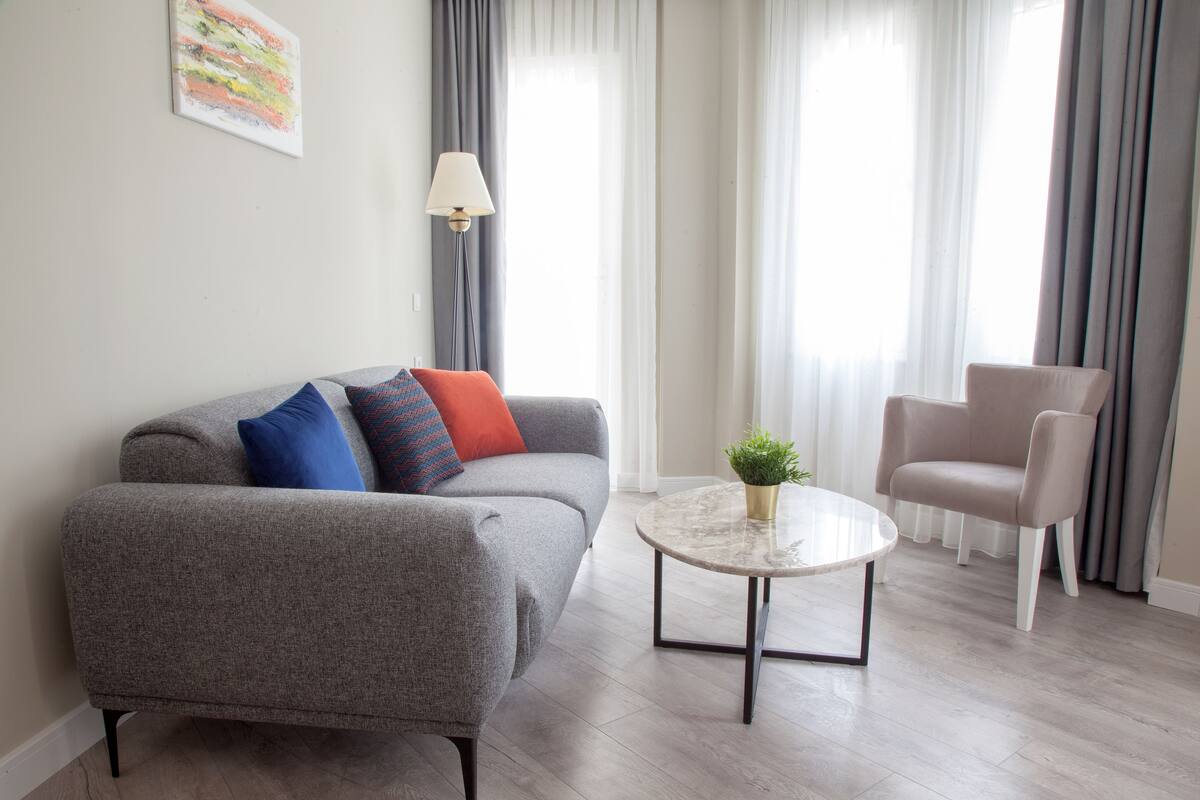 A modern living room with a grey sofa, a round coffee table, and a beige armchair.