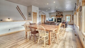 A spacious dining area with a long wooden table and chairs, a fireplace, and a cozy seating area with a couch and TV.