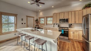 A spacious kitchen with wooden cabinets, a large island with bar stools, stainless steel appliances, and a ceiling fan.
