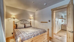 A bedroom with a wooden bed, two wall-mounted lamps, a wooden wardrobe, and a door leading to another room.